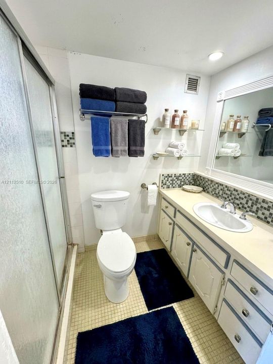Bathroom featuring a shower stall with semi-transparent enclosure, vanity with integrated sink, glass shelving, framed mirror, and mosaic tile backsplash