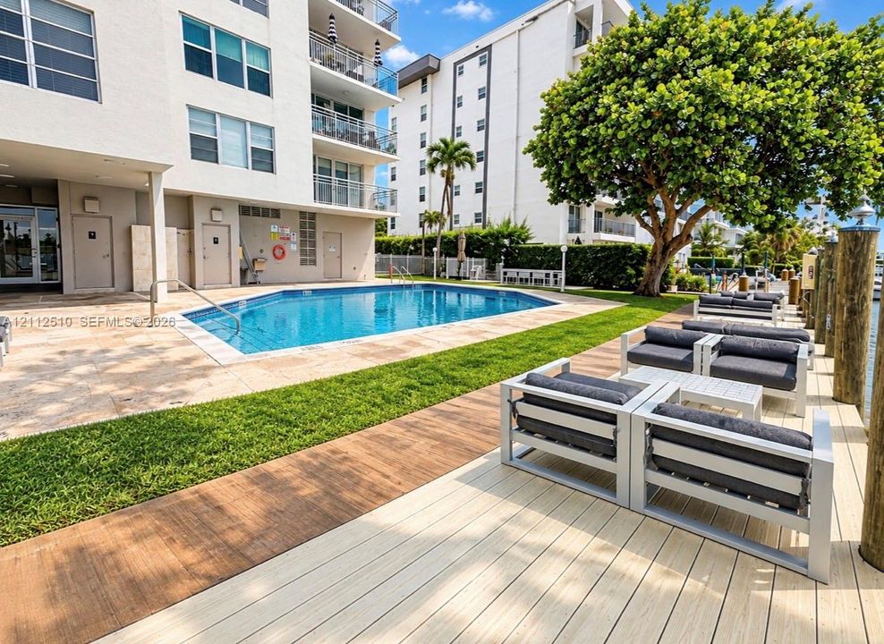 Swimming pool with a stone pool deck, wood-finish decking, and manicured lawn