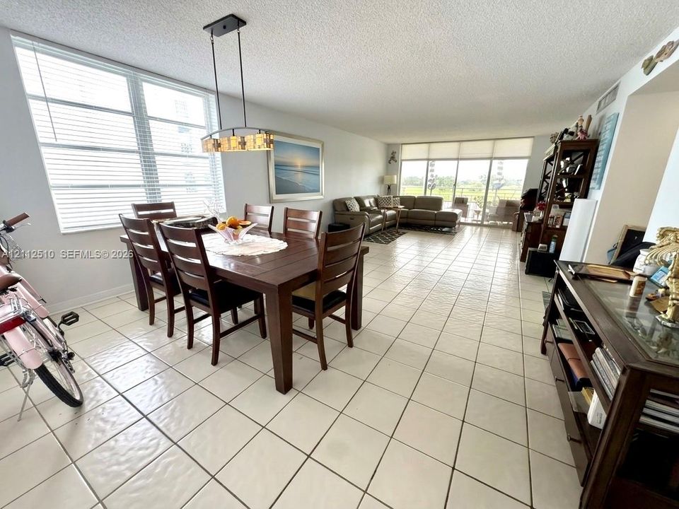 Open-concept living and dining area featuring expansive floor-to-ceiling windows, ceramic tile flooring, and a contemporary linear chandelier