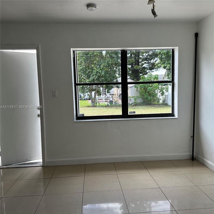 Interior space featuring light-colored tile flooring, smooth wall finishes, and a large horizontal window with black framing