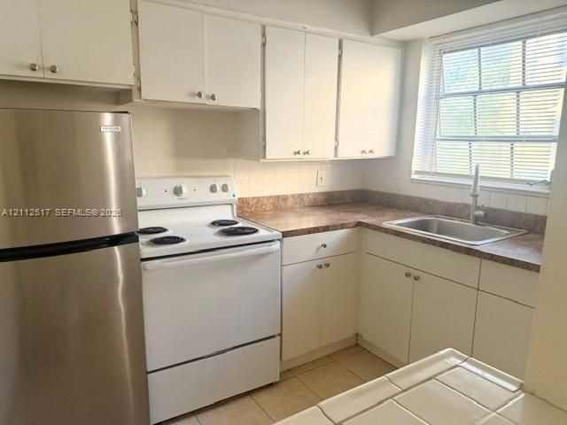 Kitchen featuring white cabinetry, stainless steel refrigerator, white electric range, laminate countertops, and tile flooring