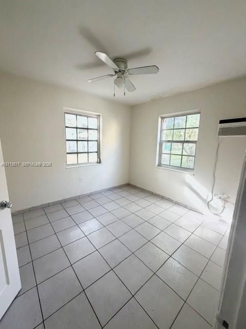 Room featuring neutral ceramic tile flooring, two grid-pane windows, a central ceiling fan with integrated lighting, and a wall-mounted cooling unit