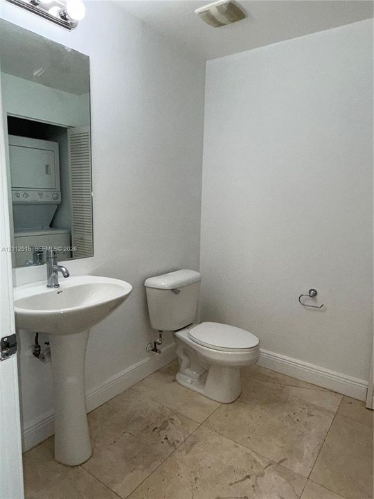 Pedestal sink with a single-handle chrome faucet, wall-mounted vanity mirror, ceramic tile flooring, and integrated laundry closet