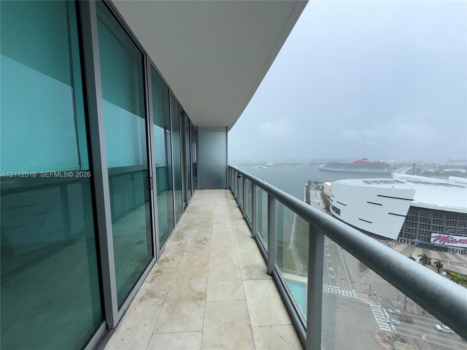 Covered balcony featuring natural stone flooring, glass railing, and floor-to-ceiling sliding glass doors