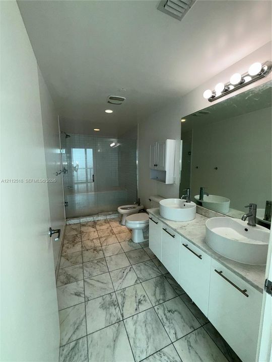 Dual-sink vanity with vessel basins, stone-surface countertop, floor-to-ceiling tile flooring, walk-in glass-enclosed shower, and wall-mounted vanity cabinetry