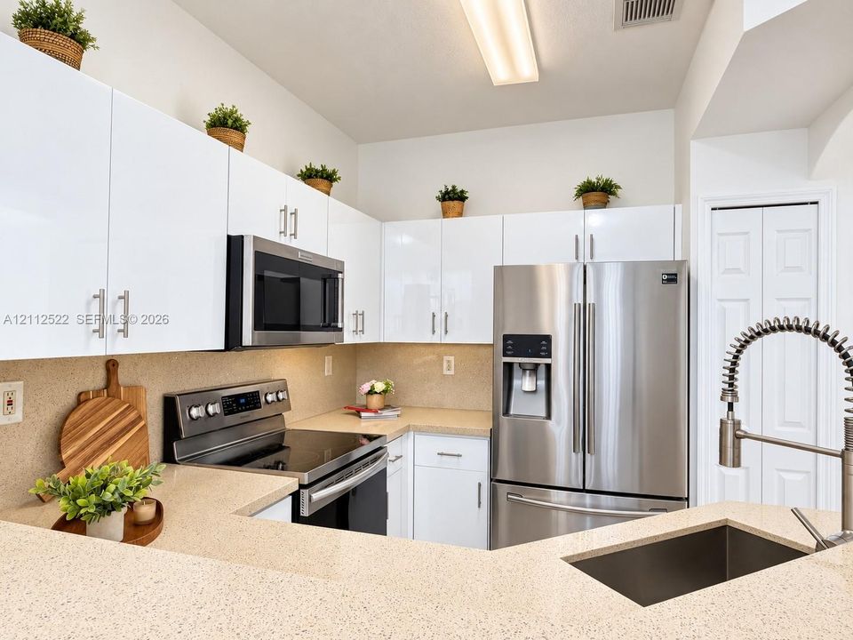 Kitchen featuring high-gloss white cabinetry, solid surface countertops, stainless steel appliances, and a gooseneck faucet with an integrated sprayer