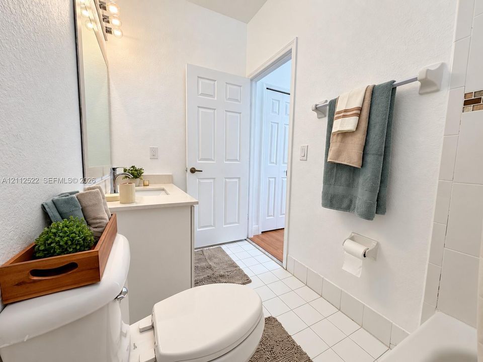 Bathroom featuring a white vanity with a rectangular sink, wall-mounted light fixture, white tile flooring, and a tiled shower surround