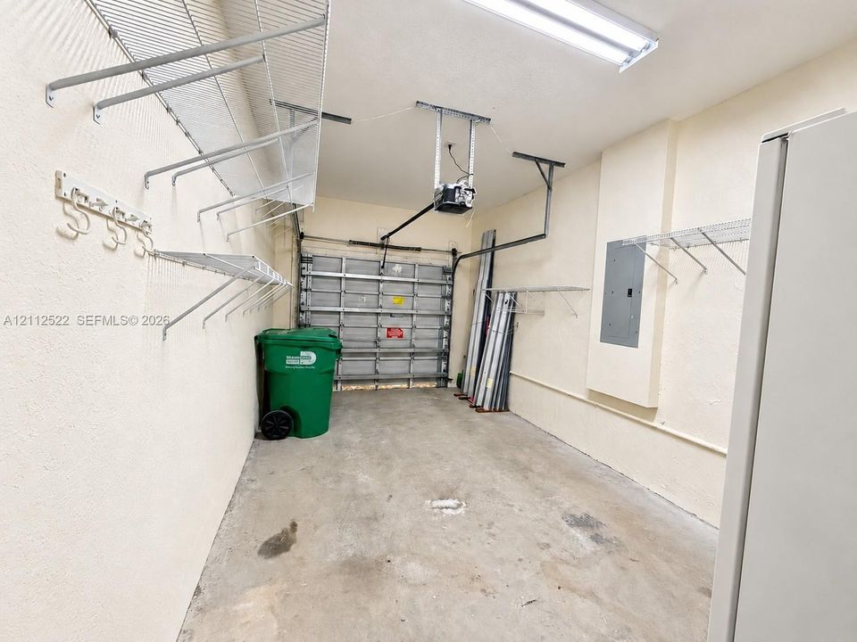 Garage interior featuring concrete flooring, a metal roll-up door, overhead fluorescent lighting, and extensive wall-mounted wire shelving