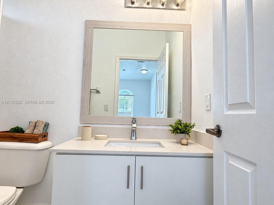 Vanity featuring a light-toned wood-finish frame mirror, stone-composite countertop, undermount sink, and minimalist hardware