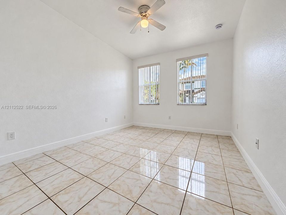 Interior room featuring large-format ceramic tile flooring, dual windows with vertical blinds, and a central ceiling fan