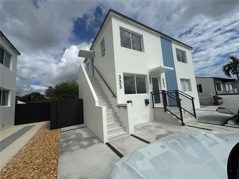 Two-story exterior featuring white stucco finish, blue vertical siding accents, concrete staircases with metal handrails, and a dedicated concrete parking area