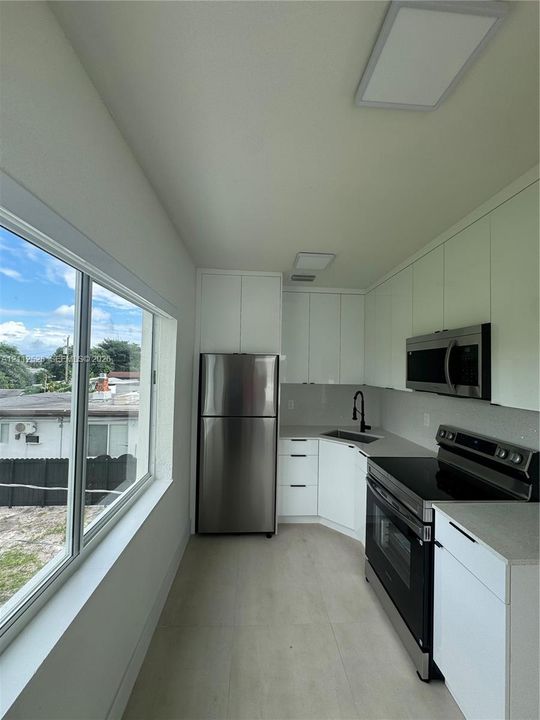 Kitchen featuring white high-gloss cabinetry, stainless steel appliances, solid-surface countertops, a matte black faucet, and expansive windows