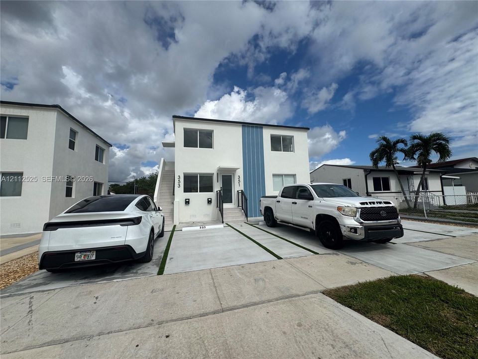 Two-story exterior featuring white stucco finish, blue vertical siding accents, concrete driveway with green space strips, and exterior staircase