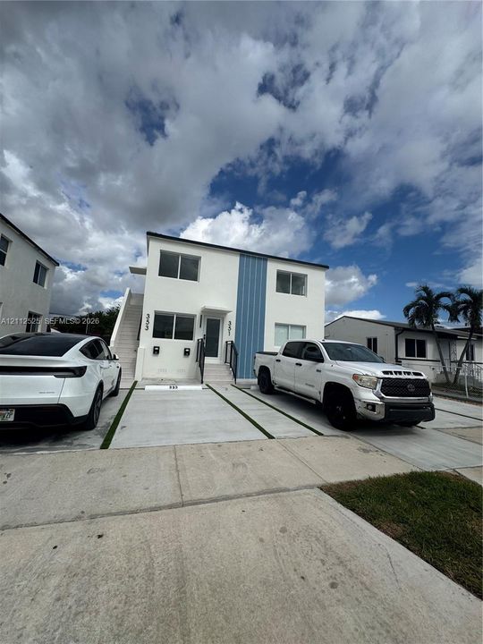 Two-story structure featuring a smooth white stucco exterior with vertical blue panel accents and designated concrete parking pads