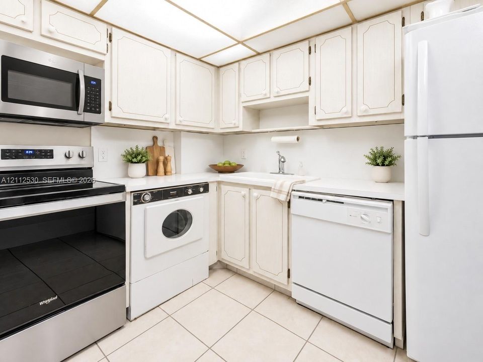 Kitchen featuring white cabinetry, integrated stainless steel and white appliances, tile flooring, and a recessed grid ceiling