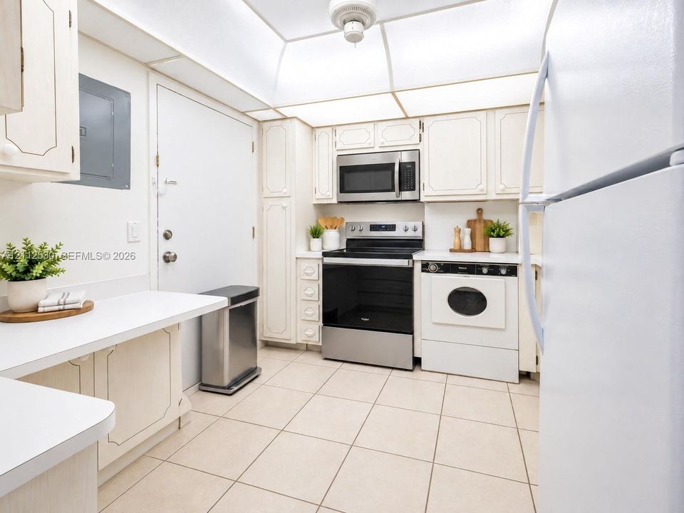 Kitchen featuring a tray ceiling with recessed lighting, tile flooring, built-in cabinetry, and integrated stainless steel and white appliances