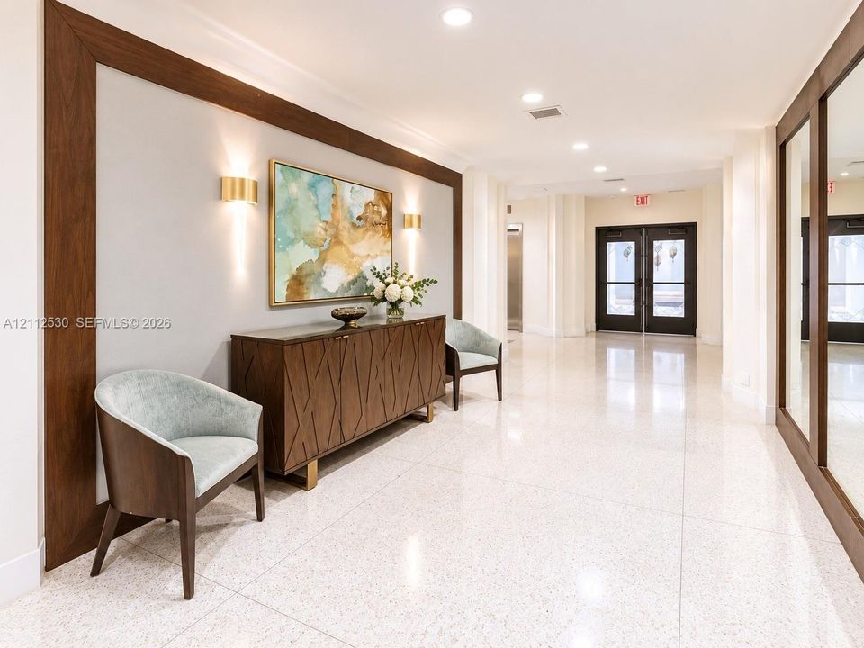 Polished stone flooring, wood-framed accent wall paneling, integrated wall-mounted lighting, and double-door entry