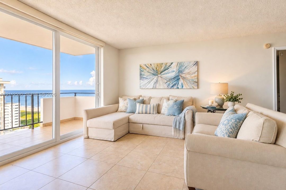 Open-concept interior featuring large-format ceramic tile flooring, floor-to-ceiling sliding glass doors, and a private balcony with ocean frontage