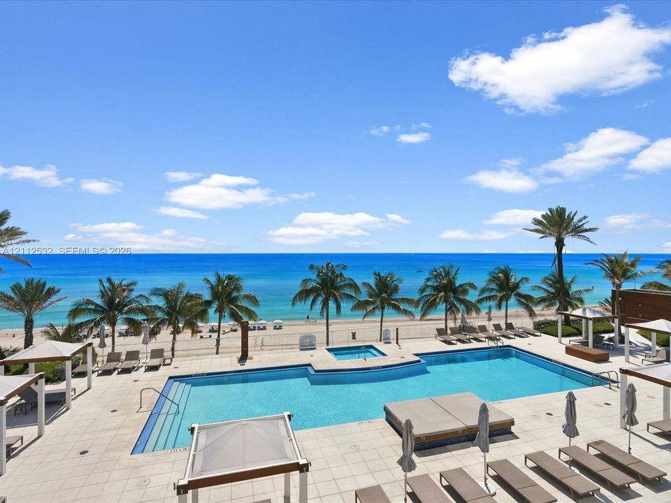 Swimming pool featuring a built-in spa, expansive stone-paver decking, and coastal horizon backdrop