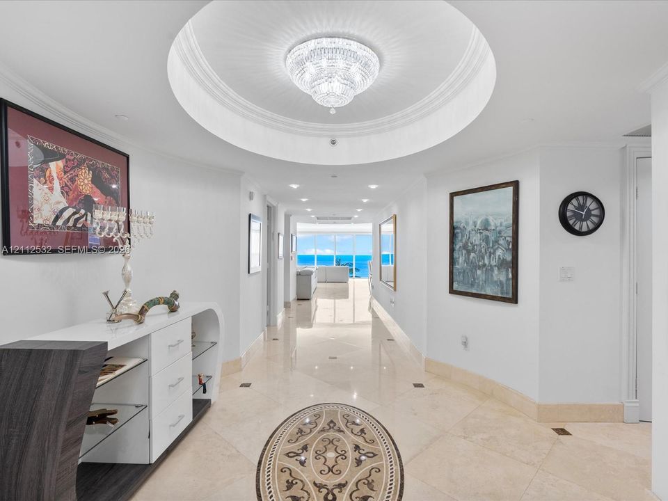 Foyer featuring a recessed circular tray ceiling, crystal chandelier, polished stone flooring with decorative inlay, and recessed lighting