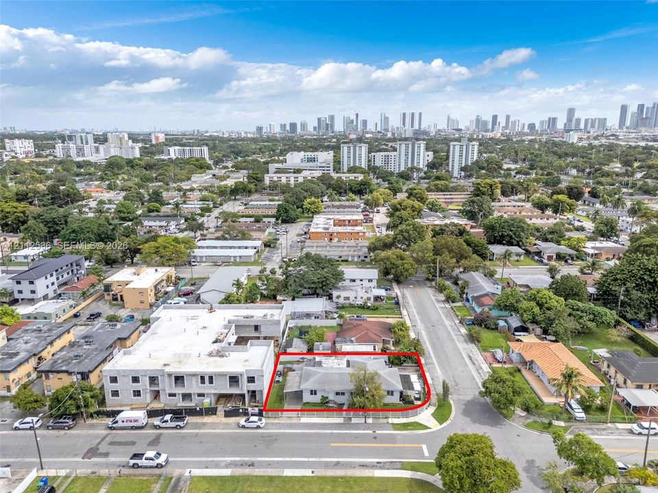Aerial perspective of a corner lot property featuring a single-story residence with a concrete driveway and paved parking area