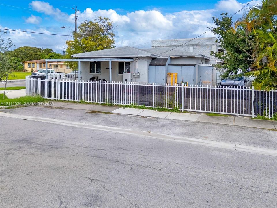 Single-story exterior featuring a covered front porch, light-toned stucco facade, and a full-perimeter metal fence
