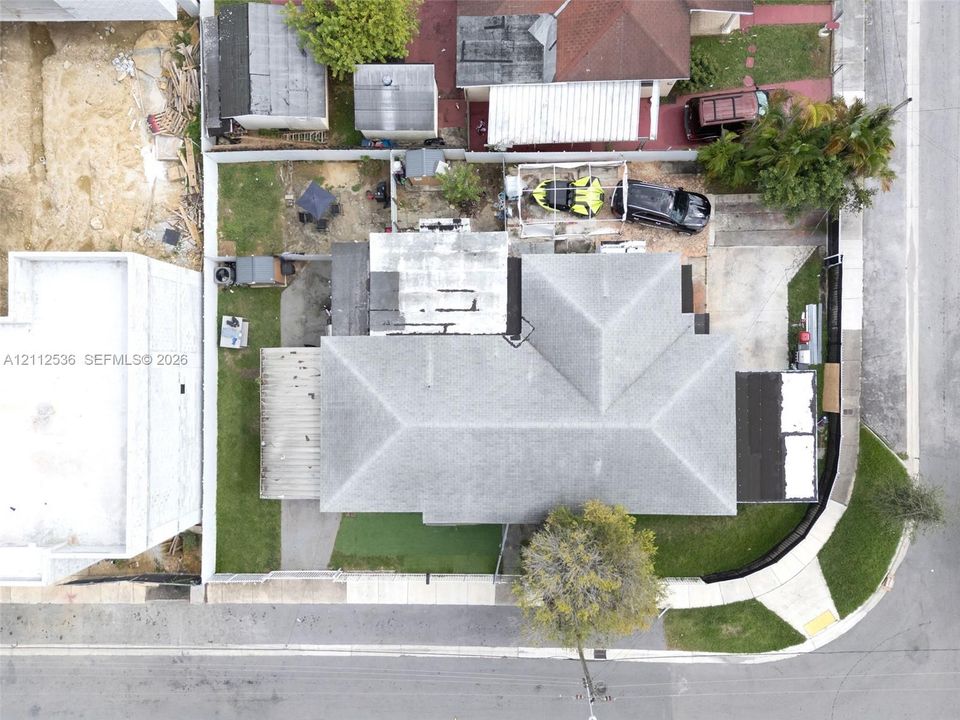 Aerial perspective of a corner lot property featuring a shingle roof, concrete driveway, perimeter fencing, and grass lawn