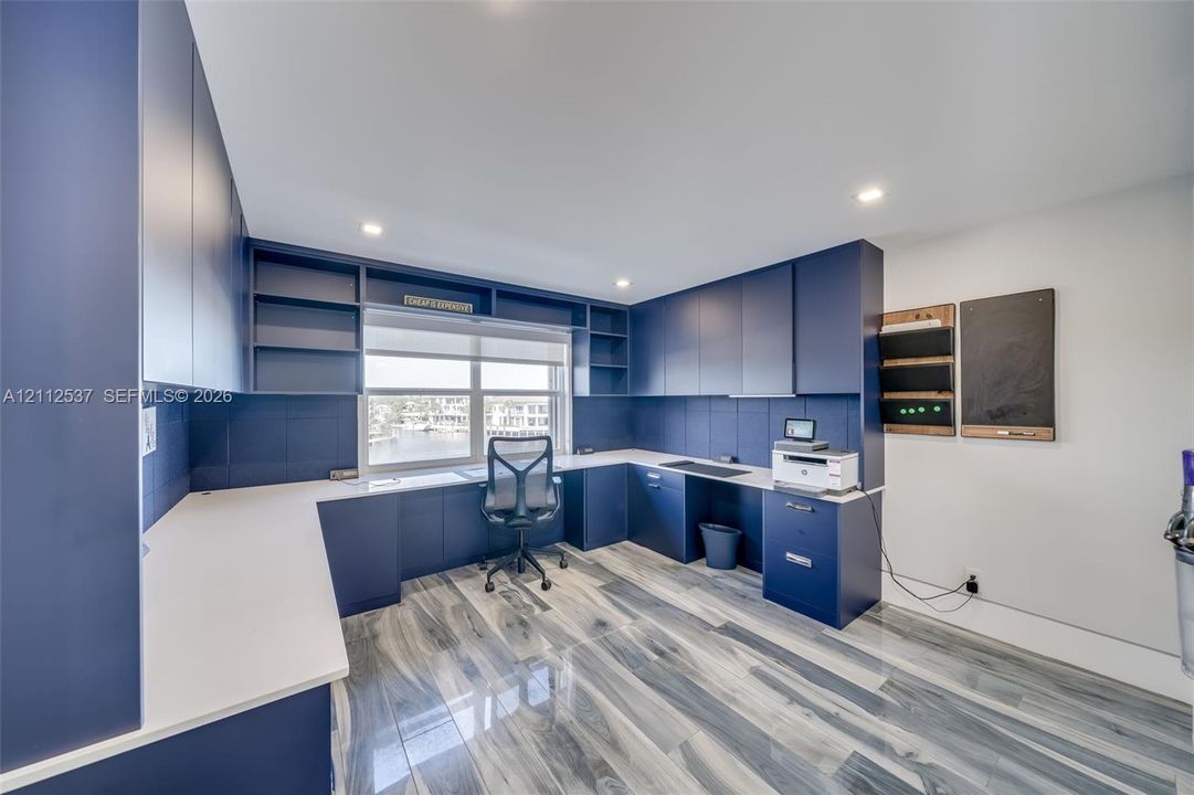 Custom built-in navy cabinetry with integrated shelving, white solid surface countertops, recessed ceiling lighting, and wood-finish flooring