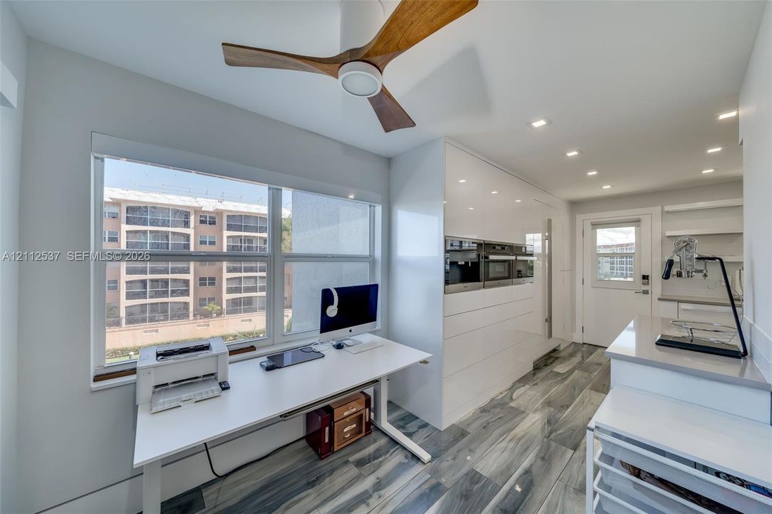 Modern kitchen featuring high-gloss white cabinetry, integrated stainless steel appliances, wood-finish ceiling fan, recessed lighting, and large-format gray patterned flooring