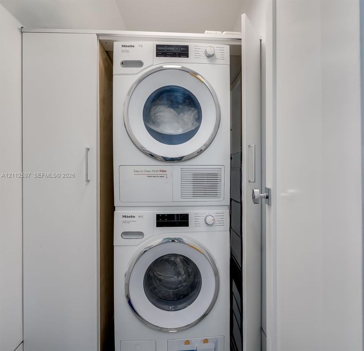 Stackable Miele washer and dryer set enclosed within custom white cabinetry featuring minimalist hardware