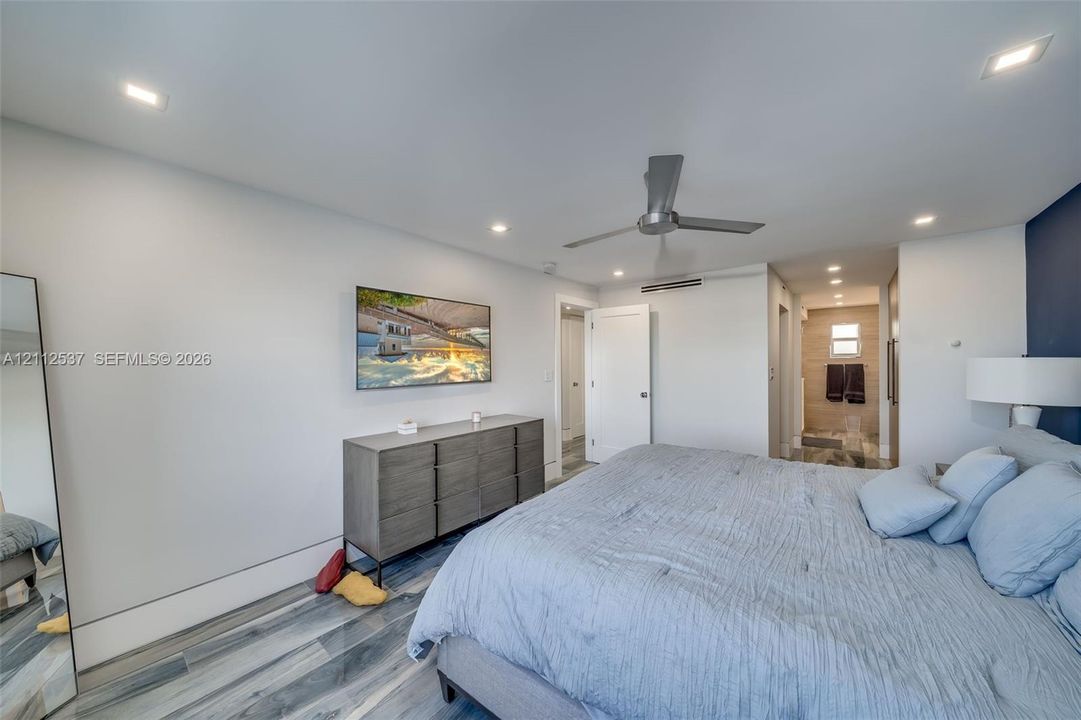 Neutral-toned room featuring wood-finish flooring, recessed LED ceiling lighting, a brushed metal ceiling fan, and an accent wall