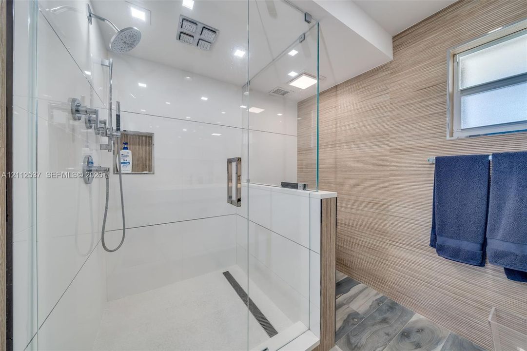 Walk-in shower featuring a glass enclosure, rainfall showerhead, handheld sprayer, built-in recessed wall niche, and wood-finish wall tile
