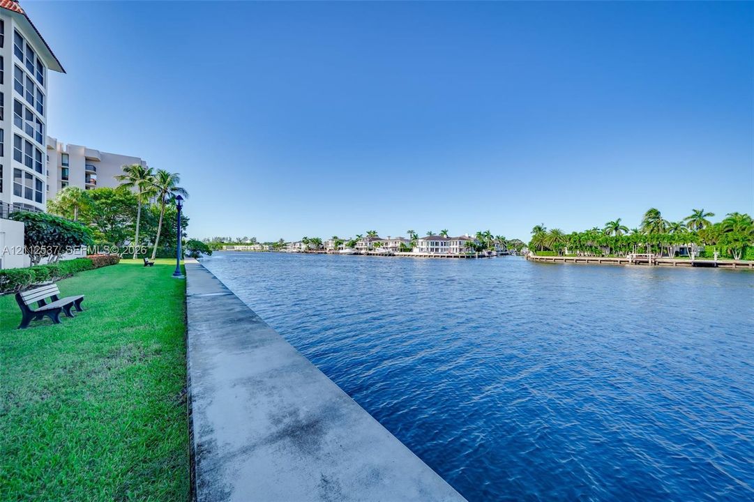 Waterfront property featuring a concrete seawall, manicured lawn, and mature palm trees