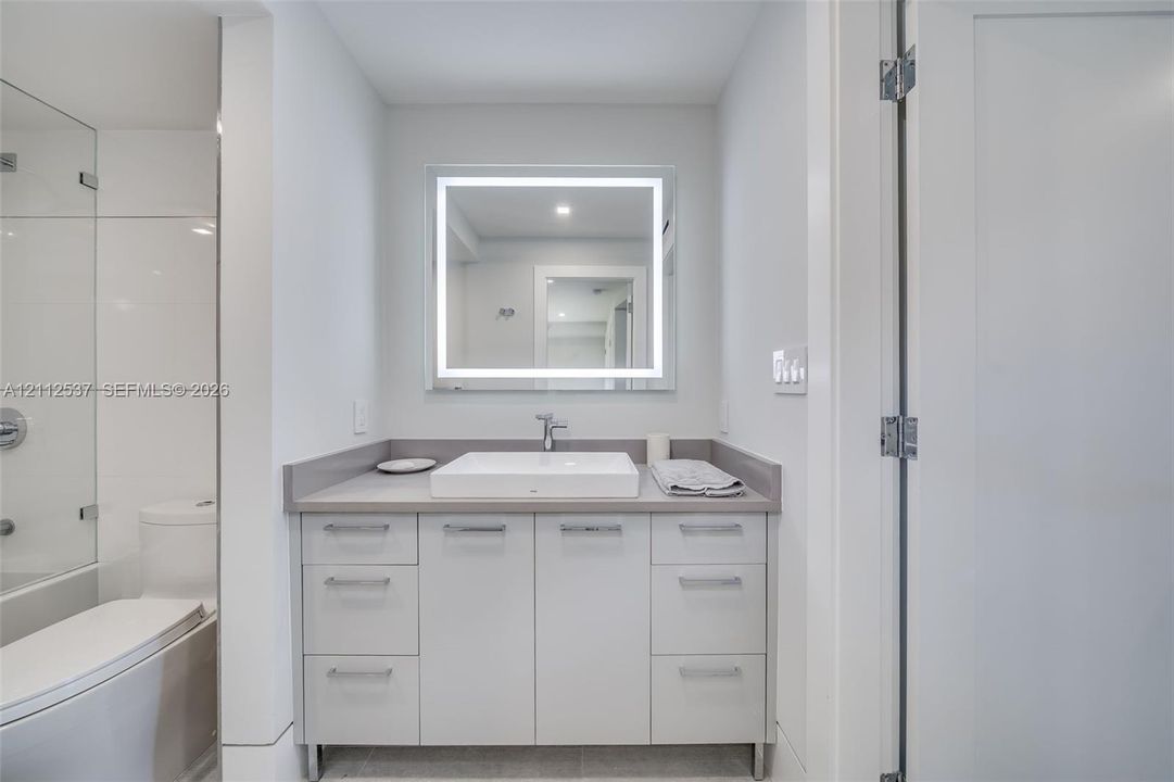 Bathroom vanity featuring flat-panel cabinetry, a rectangular vessel sink, solid-surface countertop, and an integrated LED-backlit mirror
