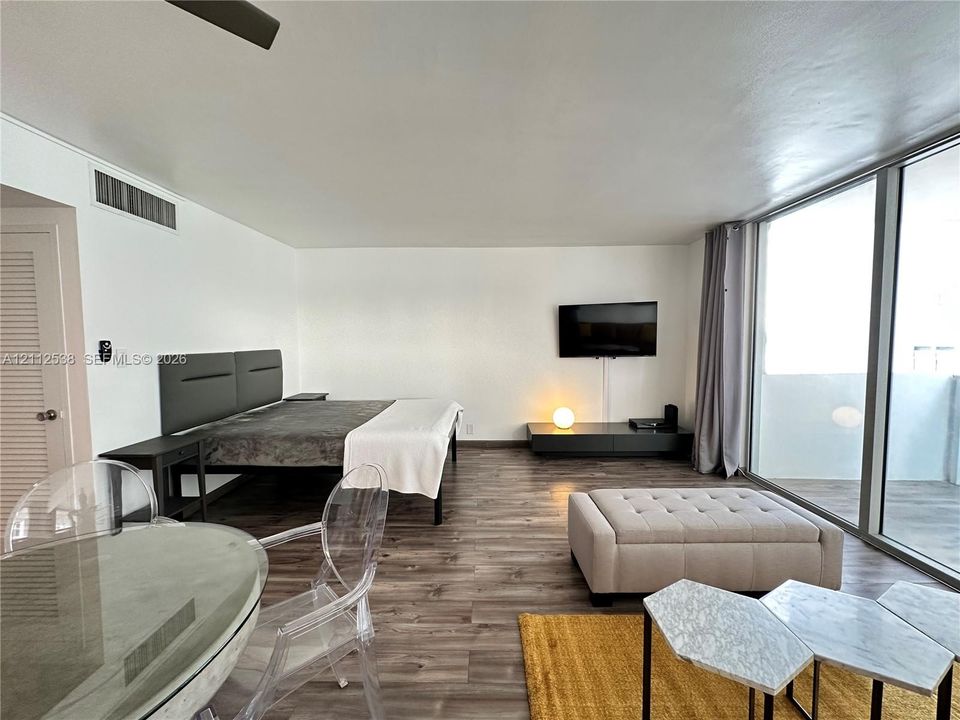 Open-concept interior featuring wood-finish flooring, floor-to-ceiling glass sliding doors, and neutral wall tones