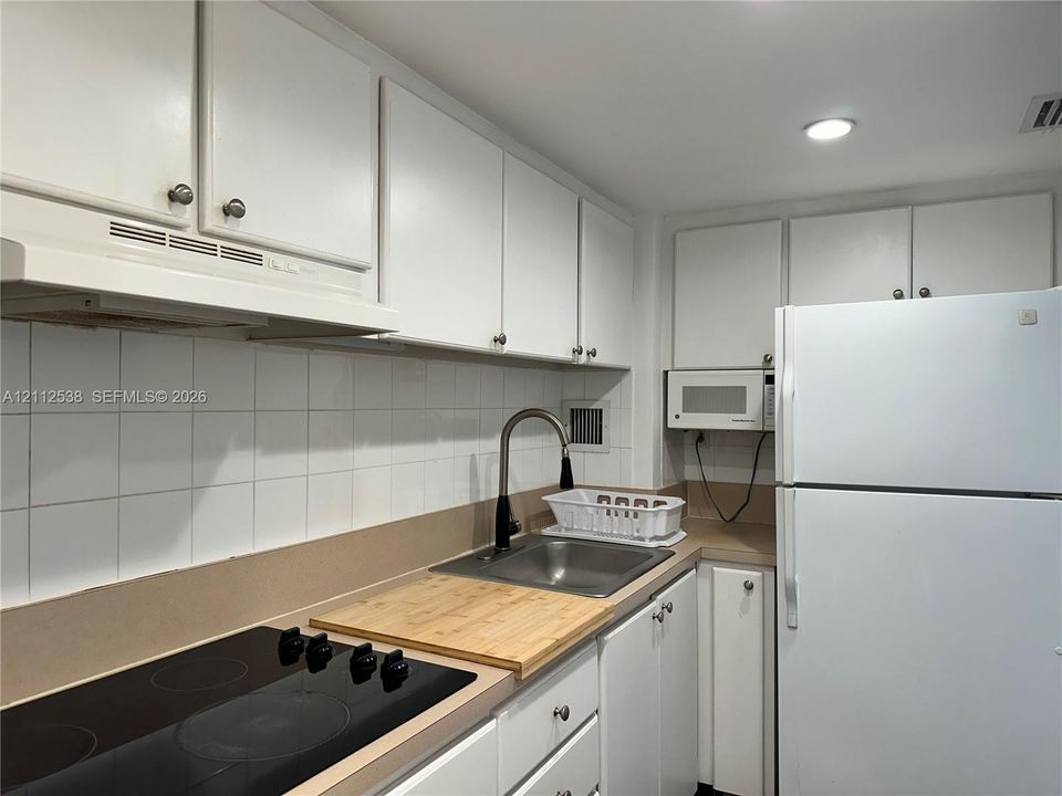 Kitchen featuring white cabinetry, solid surface countertops, square tile backsplash, stainless steel sink with high-arc faucet, and black glass cooktop