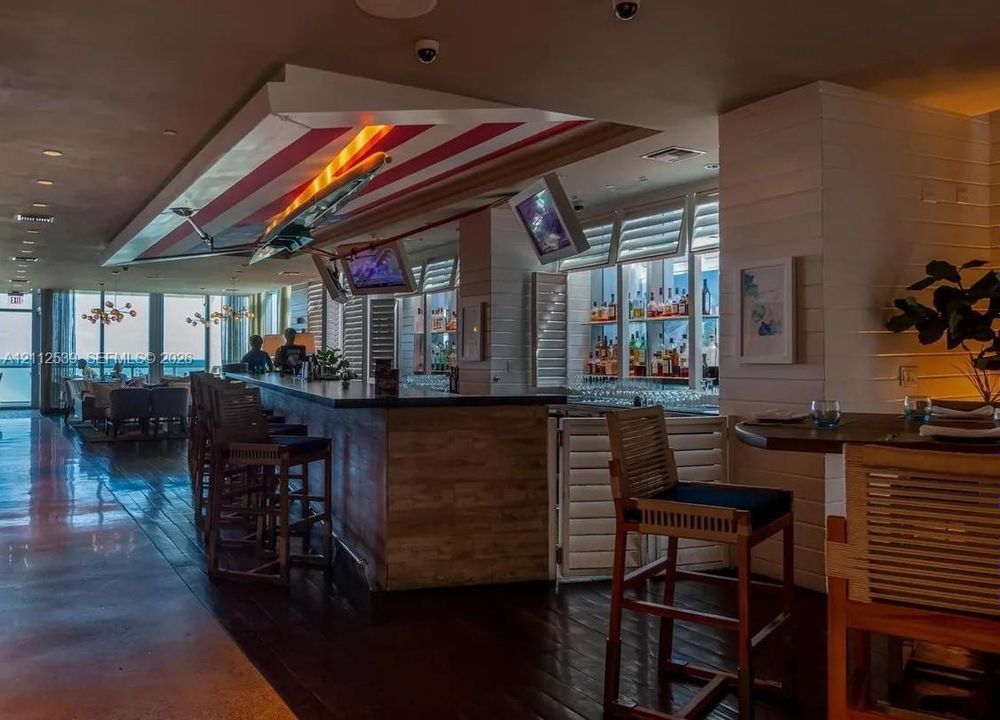 Custom bar featuring dark wood-finish flooring, built-in shelving with integrated lighting, wood-paneled counter, and louvered shutters