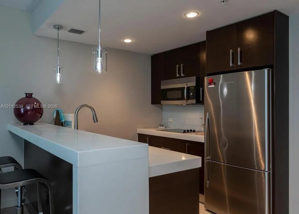 Kitchen featuring dark cabinetry, quartz countertops, stainless steel appliances, recessed lighting, and dual pendant lights