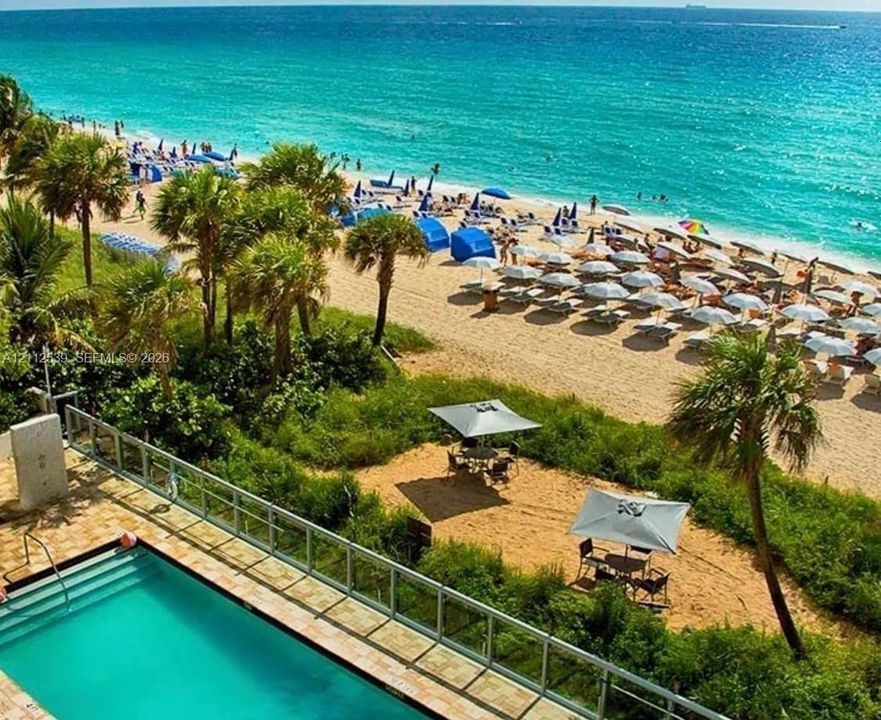 Swimming pool with stone-finish decking, glass panel railing, and direct proximity to sand dunes and the coastline
