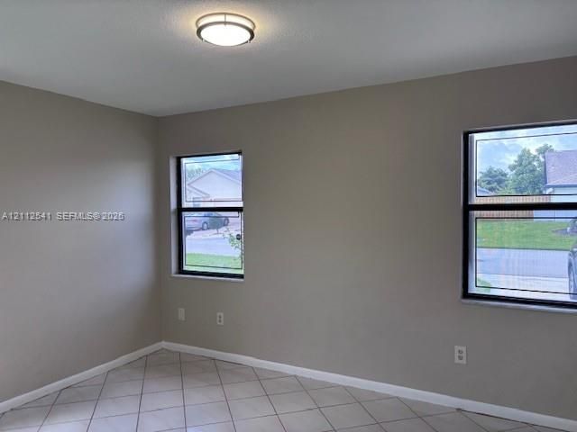 Neutral-toned interior space featuring light-colored tile flooring, flush-mount lighting, and dual windows with black frames