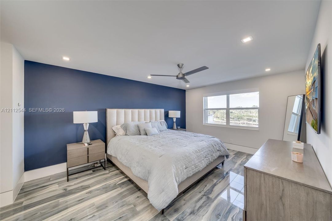 Bedroom featuring a bold navy accent wall, wood-finish tile flooring, recessed ceiling lighting, and a modern brushed-metal ceiling fan