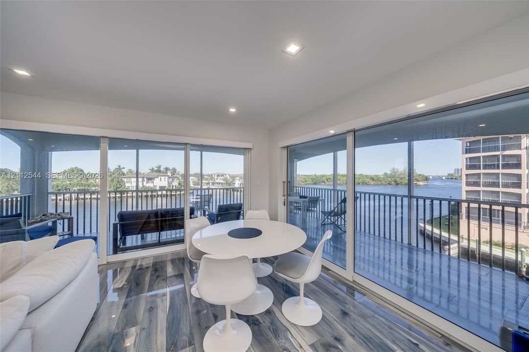 Expansive floor-to-ceiling glass sliding doors, wood-finish flooring, recessed lighting, and a wrap-around balcony with metal railing