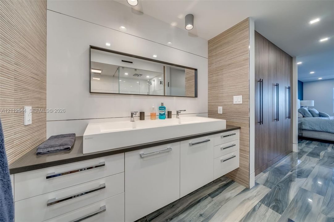 Modern floating vanity featuring a wide rectangular double-basin sink, high-gloss white cabinetry, integrated drawer pulls, wood-finish wall paneling, and recessed ceiling lighting