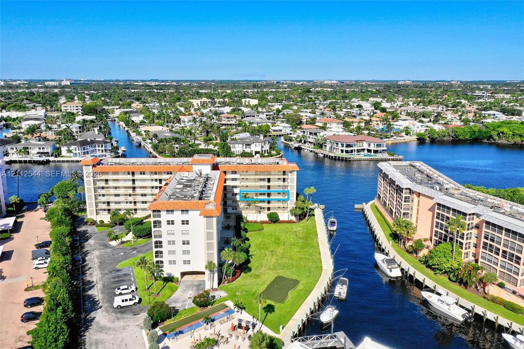 Multi-story residential building with terracotta-tiled roof, featuring water-front positioning, direct canal access, an on-site putting green, and manicured landscaping