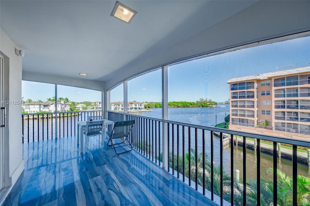 Screened balcony featuring wood-finish flooring, recessed lighting, and black metal railings overlooking the waterway