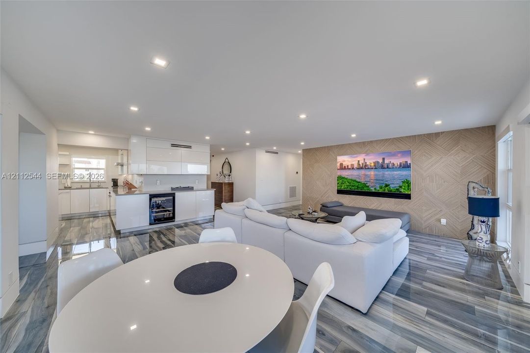 Open-concept space featuring polished stone-finish flooring, recessed lighting, glossy white cabinetry, built-in beverage refrigerator, and a decorative wood-paneled accent wall