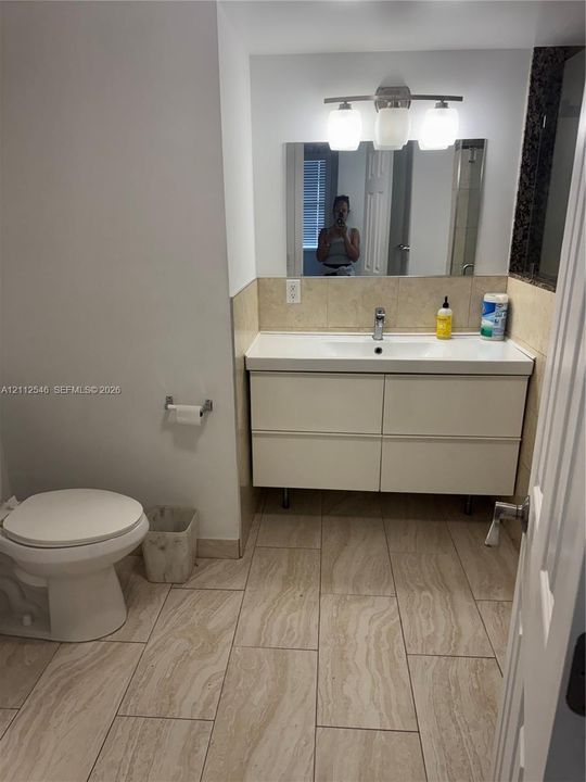 Modern floating vanity with a dual-drawer cabinet, white countertop, and polished chrome faucet, complemented by oversized neutral floor tiling and a three-light fixture