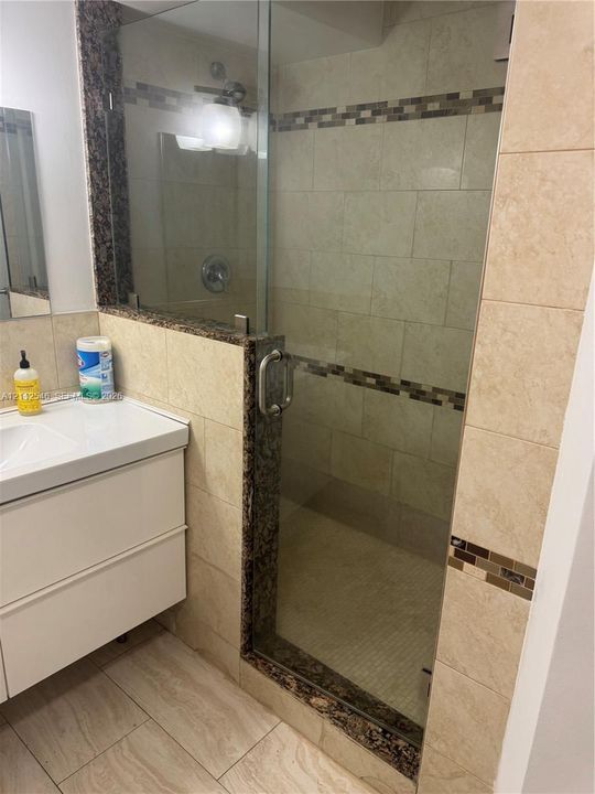 Walk-in shower with a glass door, stone-surround accents, large-format wall tiling with decorative inlay, and a white wall-mounted vanity