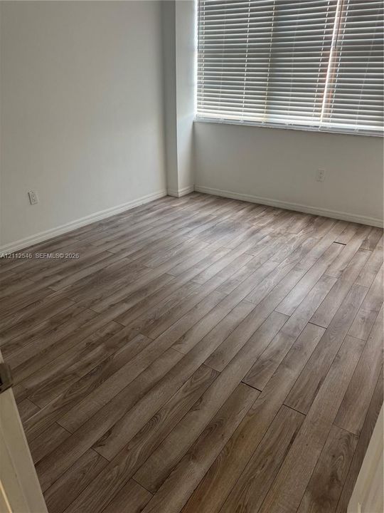 Room featuring wood-finish flooring and a large window equipped with horizontal blinds