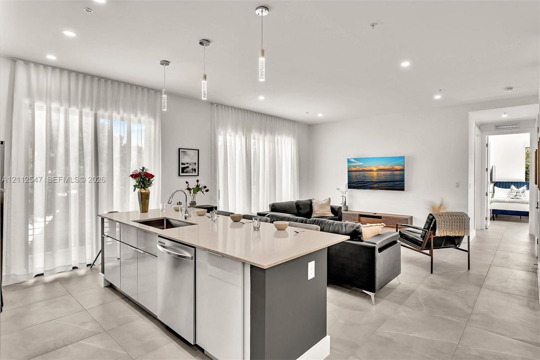 Kitchen island featuring stone countertops, stainless steel undermount sink, and integrated stainless steel dishwasher, complemented by recessed lighting and neutral tile flooring
